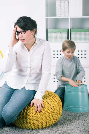 Little boy playing on bucket as a drums. Next to him his tired teacher with headacheの写真素材