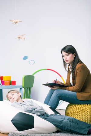 Young child psychologist and little boy refusing to talk. Sitting in nice children room