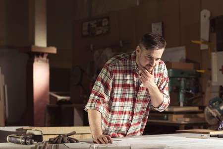 Carpenter during work in workshop, holding his chin.