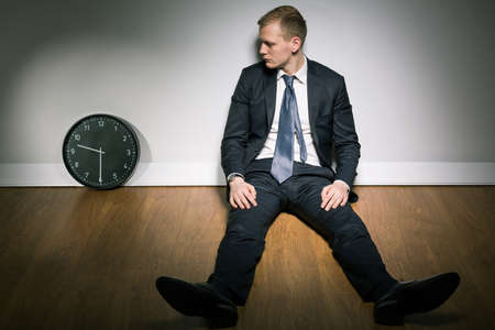 Concerned young man in suit looking at passing time on clockの写真素材