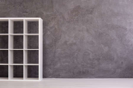 White, simple shelving unit standing in modern interior with light flooring and cement wallの写真素材