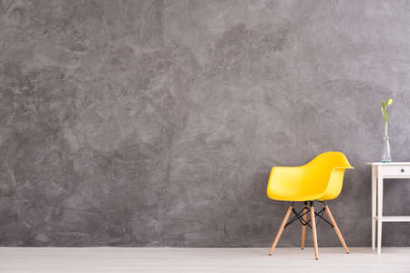 New yellow chair and small, decorative table standing in interior with grey wallの写真素材