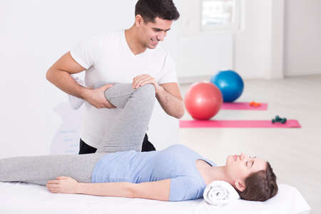 Woman during rehabilitation exercising with specialist in light interior