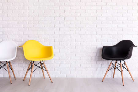 New chairs in white, yellow and black standing in white room with brick wall
