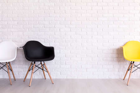 White, black and yellow chair standing in light interior with brick wall designの写真素材