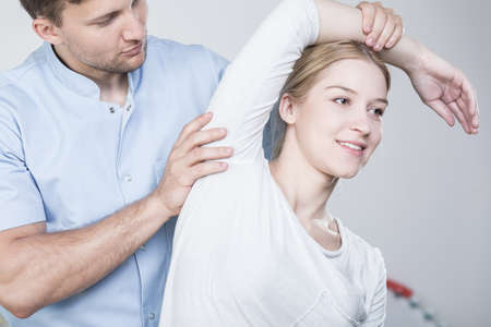 Young physiotherapist stretching woman's arm during rehabilitation