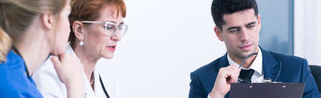 Close-up of a senior physician consulting a case with a young man and a young female doctor