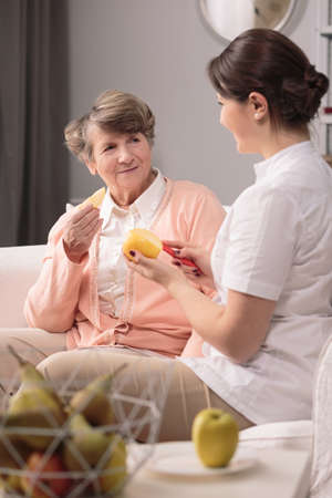 Young helpful carer peeling the orange for older woman