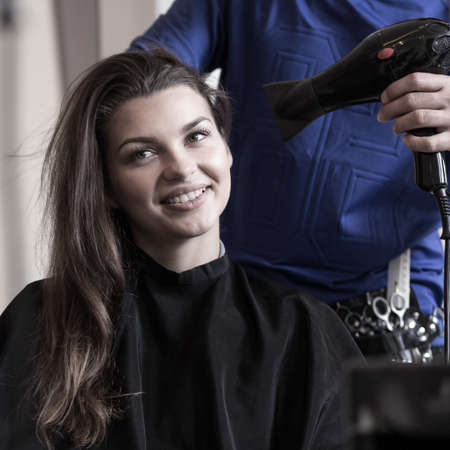 Horizontal view of hairstylist drying woman's hairの写真素材