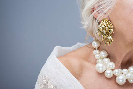 Close-up of senior elegant woman's neck with perl necklaces and ear with golden earringの写真素材