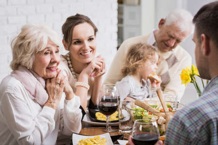 Happy family sitting beside table during dinner, granddaughter sitting on grandfather's lap