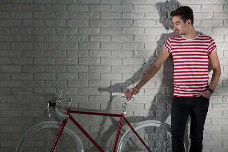 Young man and red bike, brick wall in the backgroundの写真素材