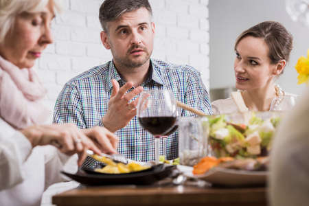 Young man and two women sitting beside table during family dinnerの写真素材