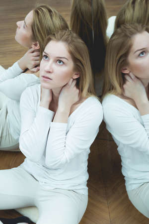 Young woman sitting on the floor of a mirrored room with her reflections behind her backの写真素材