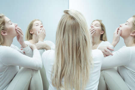 Shot of a young woman dressed in white sitting in circle of multiple reflections of her own with her...