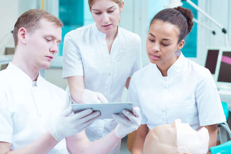 Young male handsome medicine student showing two friends his work on tabletの写真素材