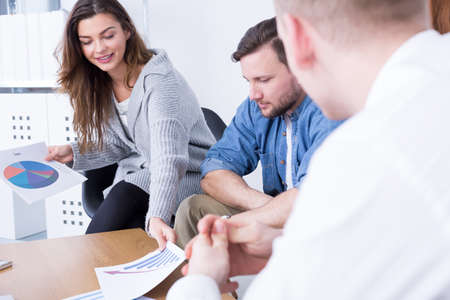 Woman and two young men sitting beside table at modern office
