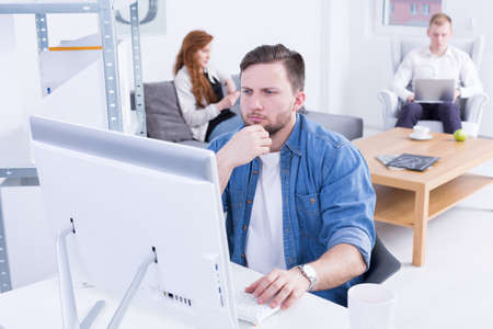 Young man sitting beside desk, using computer at modern office