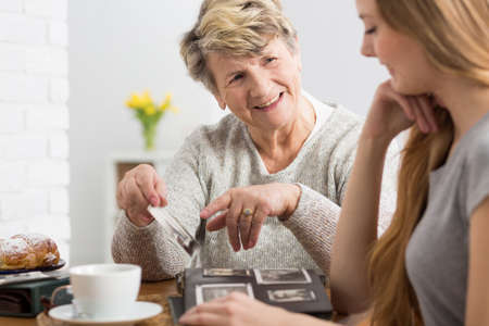 Senior woman holding picture, watching photo album with her granddaughterの写真素材