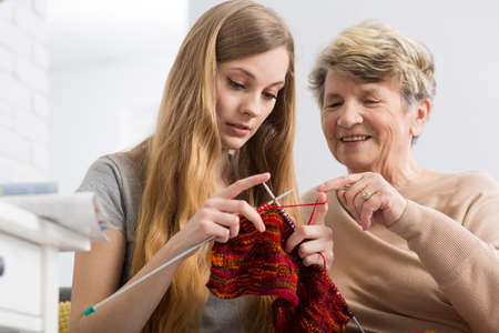 Happy grandmother teaching her granddaughter knitting, smilingの写真素材