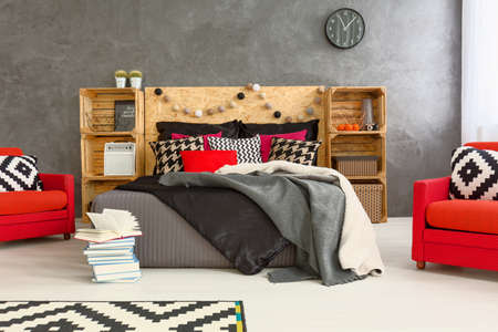 Spacious bedroom in grey with double bed, DIY regales, pattern details and two, red armchairsの写真素材
