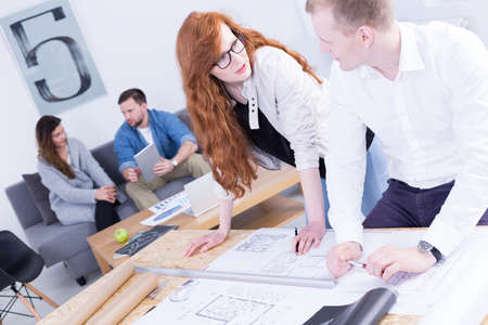 Young man and woman discussing project, standing beside desk in light, modern officeの写真素材