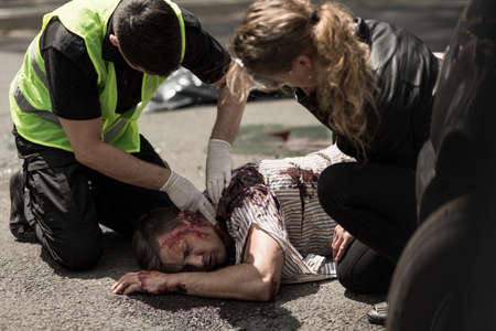 Man and woman giving first aid to injured man lying on street.の写真素材