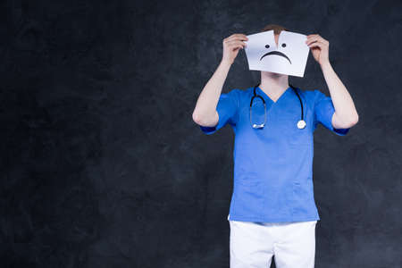 Shot of a young doctor tearing up a piece of paper with a sad face on itの写真素材