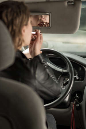 Woman back view driving a car, coloring lips with lipstick