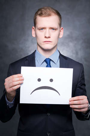 Shot of a serious young man holding a paper with a sad face on itの写真素材