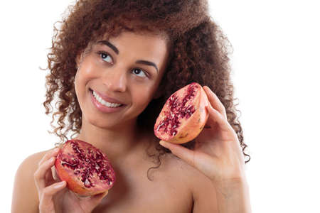 Portrait of an afroamerican woman holding two pieces of a pomegranate, smiling, white backgroundの写真素材