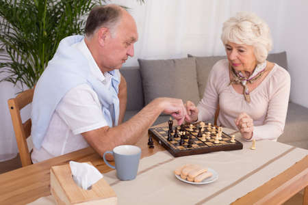 Older focus couple playing chess at home in the evening. On the table snack and teaの写真素材