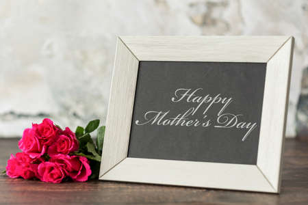 Shot of a frame saying 'Happy Mother's day' and a bunch of pink roses laying next to itの写真素材
