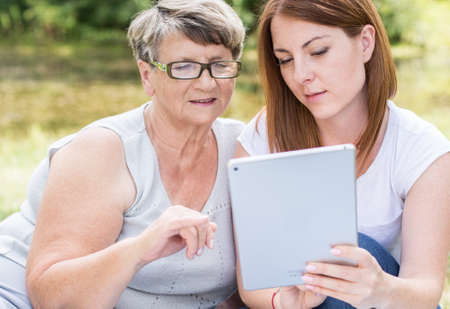 Outdoor portrait of a young woman with her grandmother, watching something at a tabletの写真素材