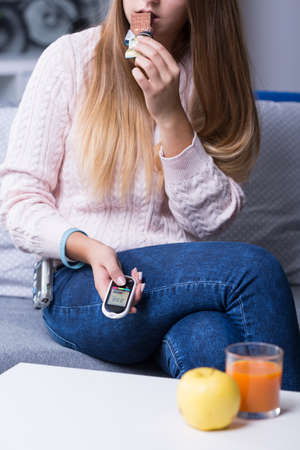 Diabetic woman golding glucometer, eating snack.の写真素材