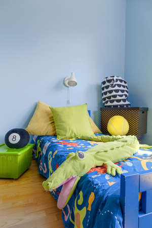 Corner of a teenager room in blue, with bed decorated with mascot crocodile and cushionsの写真素材
