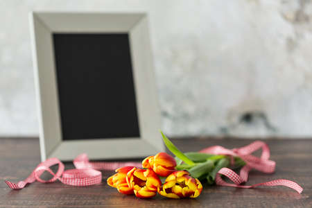 Close up of a frame, tulips and red ribbon lying on wooden tableの写真素材