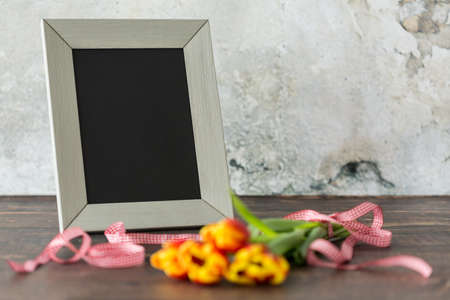 Close up of bouquet of flowers, red pattern ribbon and frame lying on wooden tableの写真素材
