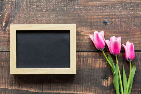 Empty wooden frame and three pink tulips lying on wooden boardの写真素材