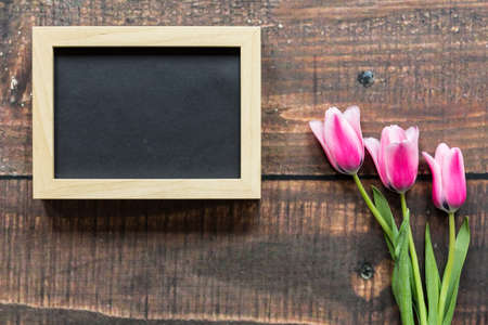 Three pink tulips and empty wooden frame lying on rustical planksの写真素材