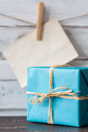 Blue, wrapped gift and empty card hanging on a string, light planks in the backgroundの写真素材