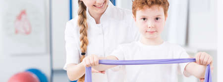 Little boy doing an exercise with the help of pediatric physiotherapistの写真素材