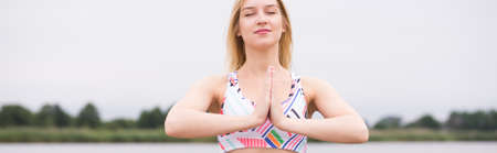 Young girl with closed eyes doing morning yoga at lakeの写真素材