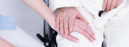 Close-up of older disabled patient holding her young caregivers handの写真素材