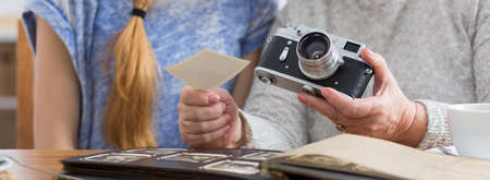 Cropped picture of an elder woman holding a camera and showing old photographs to her granddaughterの写真素材