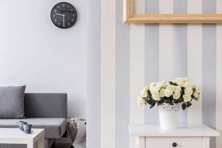Bright, modern living room with roses in a flowerpot on a white table in the foreground