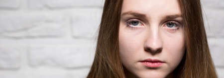 Very sad young girl, light brick wall in the background, panoramaの写真素材