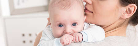 Close-up panoramic portrait of an infant held by his mother on her shoulder, clenching his little...