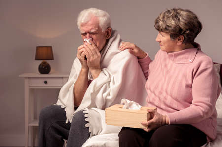 Ill senior man and his caring wife sitting in a cozy home interiorの写真素材
