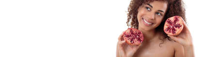Beautiful young woman with dark smooth skin holding two halves of juicy grenadeの写真素材